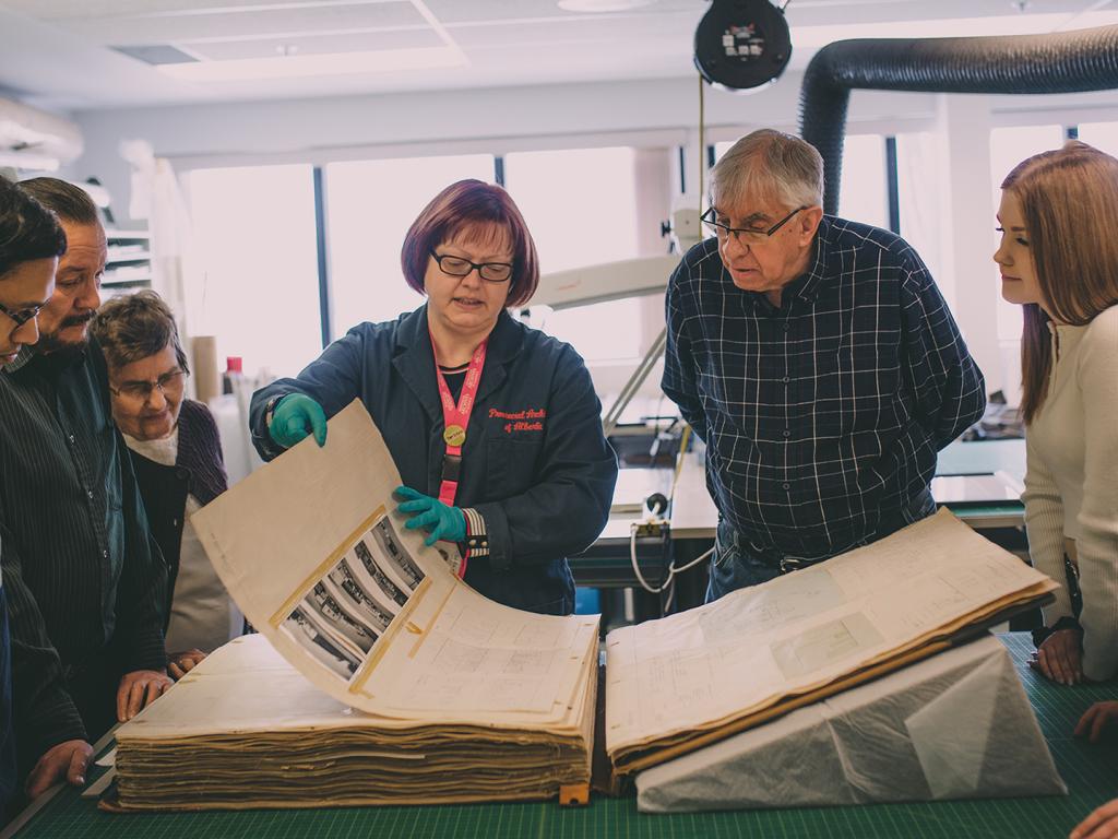 Conservator examining large book with a number of visitors